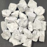 Grosse collection de pierres de marbre blanc brut, naturelles, avec veines grises, disposées sur une surface noire. Parfaites pour décoration ou projets artistiques.