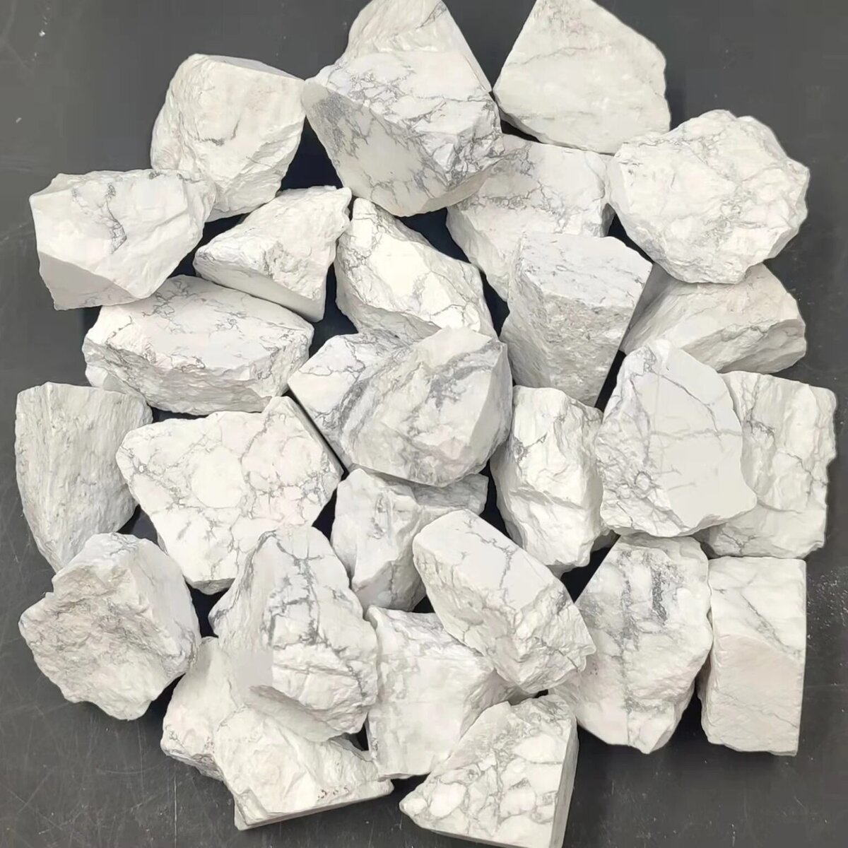 Grosse collection de pierres de marbre blanc brut, naturelles, avec veines grises, disposées sur une surface noire. Parfaites pour décoration ou projets artistiques.