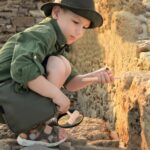 Enfant curieux utilisant une loupe pour examiner des pierres anciennes lors d'une exploration en plein air.