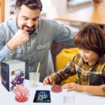 Image montrant un adulte et un enfant réalisant une expérience scientifique avec des cristaux colorés et un smartphone, dans un environnement éducatif et ludique.