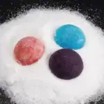 Balais de savon colorés en boule sur poudre blanche.