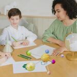 Jeune fille et garçon étudiant avec des modèles planétaires en papier sur une table, illustrant l'apprentissage de l'astronomie et la science pour enfants.