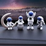 Quatre figurines d'astronautes en décoration, avec un décor lunaire et montagneux en arrière-plan, parfaites pour une décoration thématique scientifique ou spatiale.