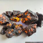 Pierre de météorite incandescente avec une surface rugueuse et des éclats lumineux orange, illustrant un phénomène naturel spectaculaire.