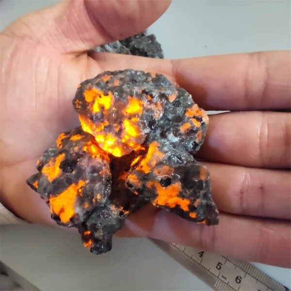 Météorite avec surface noire et éclats lumineux orange, illuminée par une lumière interne, tenue dans une main humaine pour montrer sa taille.