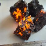 Fragment de météorite avec surfaces brillantes et éclats lumineux orange, illustrant la composition extraterrestre.
