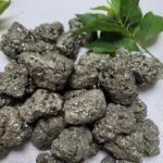 Groupe de pierres de pyrite avec éclats métalliques brillants, accompagnées de feuilles vertes, sur fond neutre. Parfait pour décoration scientifique ou collection minéralogique.