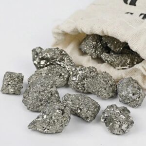 Pépite de pyrite brillante et métallique, provenant d'une collection scientifique, disposée sur une surface blanche avec un sac en toile en arrière-plan.