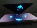 Méduse fluorescente en suspension dans une vitrine noire, illuminée par une lumière bleue, créant un effet visuel captivant et mystérieux.