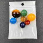 Billes de marbre multicolores, en verre, dans un sac plastique transparent, utilisées comme objets de décoration ou pour des jeux éducatifs.