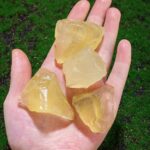 Quatre morceaux de savon de laboratoire translucides de couleur jaune clair, tenus dans une main contre un fond de pelouse verte.