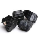 Quatre cristaux de tourmaline noire bruts, présentant une texture striée et une couleur sombre, utilisés comme objets de décoration ou pour la lithothérapie.