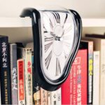 Un reloj de pared con diseño de reloj derretido, colocado entre libros en una estantería.