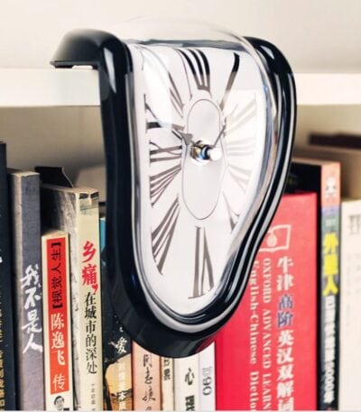 Un reloj de pared con diseño de reloj derretido, colocado entre libros en una estantería.