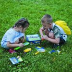 Deux enfants jouent avec des outils scientifiques dans un parc vert, découvrant la nature et la science avec curiosité et enthousiasme.