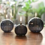 Bougies en forme de sphère en verre noir avec flamme allumée, décoratives et originales.