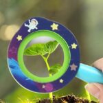 Image d'une main tenant un microscope pour observer une jeune plante en croissance dans la terre.