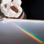 Pince tenant un prisme optique créant un arc-en-ciel de lumière sur une surface lisse, illustrant la dispersion de la lumière.
