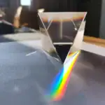 Pyramide en cristal transparent créant un arc-en-ciel de lumière sur la surface. Objet scientifique décoratif, parfait pour une décoration de style scientifique ou moderne.