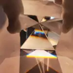 Pyramide en cristal avec refraction de lumière, créant un arc-en-ciel coloré sur une surface en bois.