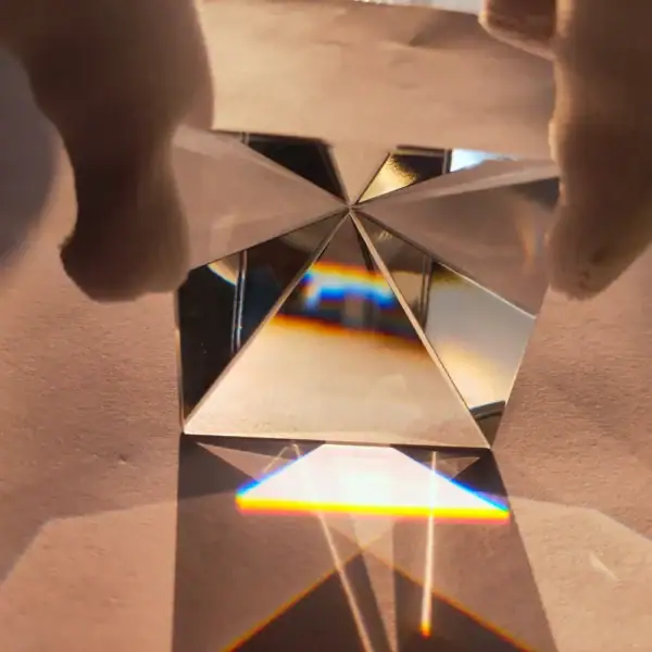 Pyramide en cristal avec refraction de lumière, créant un arc-en-ciel coloré sur une surface en bois.