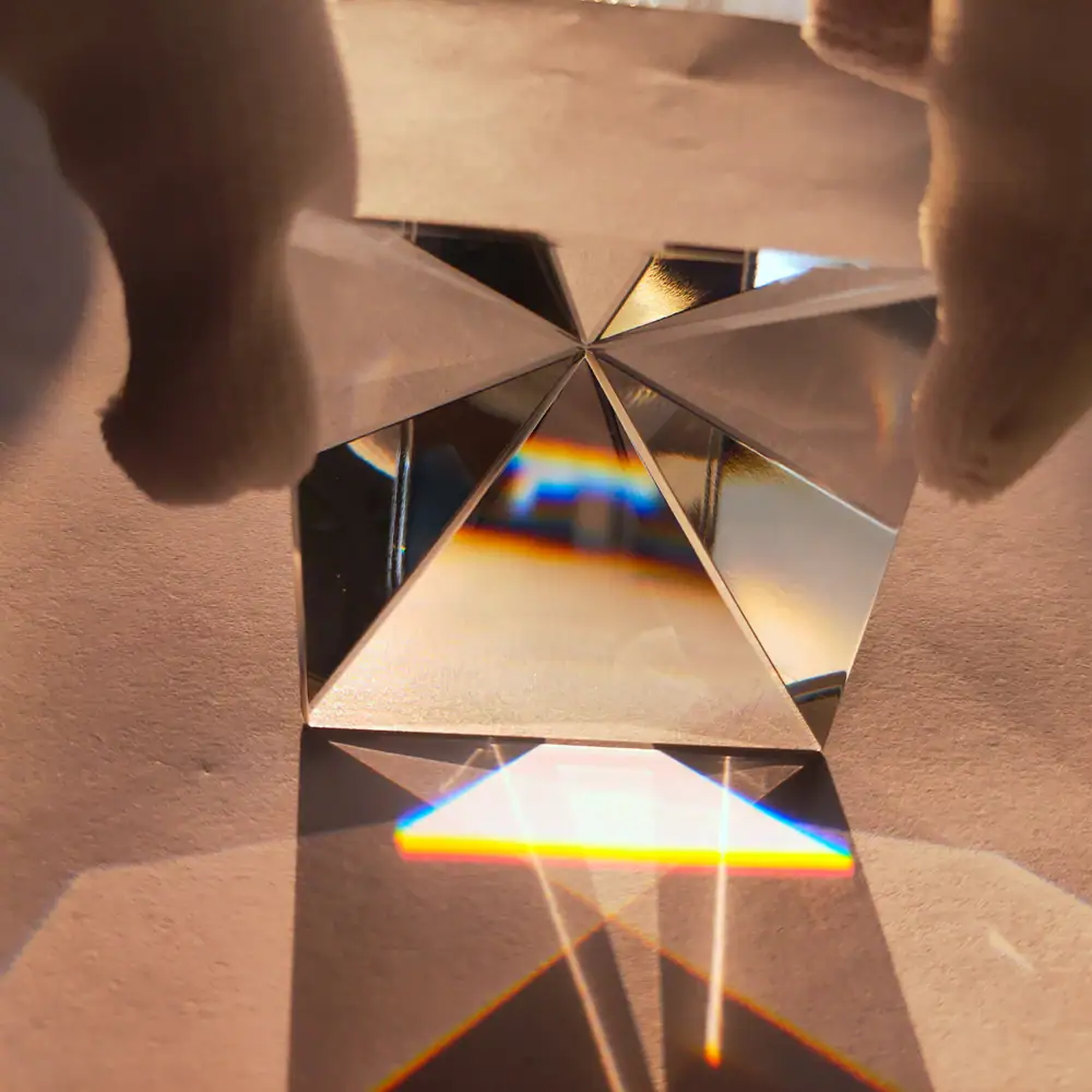 Pyramide en cristal avec refraction de lumière, créant un arc-en-ciel coloré sur une surface en bois.