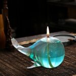 Sculpture en verre représentant une baleine avec une bougie allumée à l'intérieur, posée sur une surface en bois.