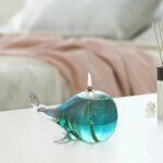 Lampe décorative en forme de baleine en verre coloré avec flamme allumée, idéale pour la décoration scientifique ou enfantine.