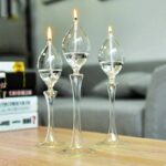 Trois vases en verre transparents avec bougies allumées, décorant une table en bois dans un intérieur moderne.