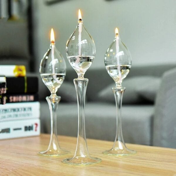 Trois vases en verre transparents avec bougies allumées, décorant une table en bois dans un intérieur moderne.