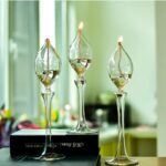 Trois vases en verre en forme de flamme avec bougies allumées, posés sur une surface dans une cuisine lumineuse.