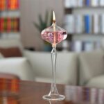 Vase à bougie en verre avec liquide rose et flamme allumée, décor scientifique élégant.