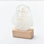 Pierre à écriture en verre avec inscriptions anciennes gravées, posée sur un socle en bois, décoration scientifique unique et élégante.