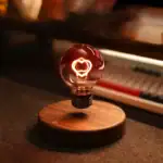 Ampoule décorative en verre avec filament en forme de cœur, éclairée d'une lumière chaude, posée sur une base en bois.