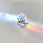 Petite boule de cristal avec reflet arc-en-ciel projetant une lumière colorée sur une surface blanche, créant un effet visuel captivant et mystérieux.