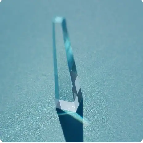 Pointe de cristal bleue translucide, posée sur un fond bleu clair, mettant en valeur sa transparence et ses reflets lumineux.