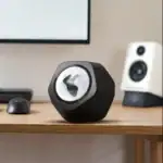 Petit pupitre de laboratoire avec logo scientifique, placé sur un bureau en bois, avec un écran d'ordinateur et une enceinte en arriÚre-plan.