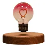 Ampoule cœur en verre rose avec filament lumineux en forme de cœur, posée sur un socle en bois naturel. Idéal pour décoration romantique ou scientifique.