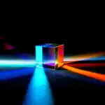 Cube en verre transparent illuminé par des lumières multicolores, créant des reflets vibrants et un jeu de couleurs sur une surface sombre.