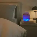 Lampe en pierre naturelle avec lumière LED bleue, posée sur une table de chevet à côté d'un lit, créant une ambiance relaxante et moderne dans la chambre.