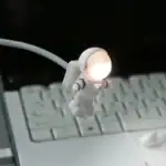 Petit robot lumineux blanc avec corps articulé, éclairant sa tête, posé sur un clavier d'ordinateur, parfait pour une décoration thématique scientifique ou technologique.