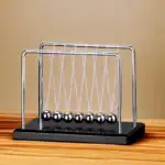 Penduim Newton avec sphères métalliques suspendues, modèle classique pour démonstration physique, posé sur une surface en bois clair.