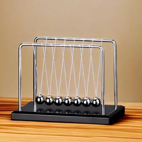 Penduim Newton avec sphères métalliques suspendues, modèle classique pour démonstration physique, posé sur une surface en bois clair.
