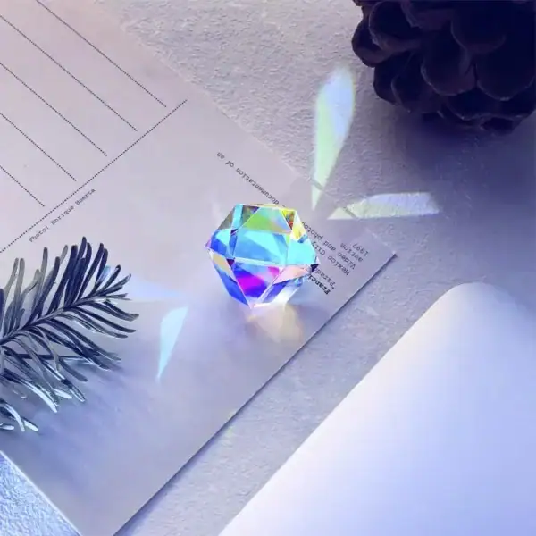 Pierre précieuse en verre irisé avec reflets colorés, posée sur une feuille blanche, entourée d'une branche de pin et d'une boule noire, lumière naturelle.