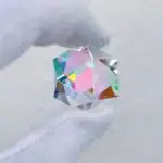 Pierre en verre optique avec reflets colorés, tenue délicate entre les doigts.