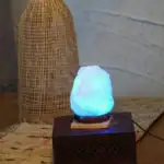 Lampe en cristal de roche illuminée avec une lumière bleue douce, posée sur un socle en bois, décorant un intérieur avec un style naturel et élégant.