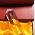 Pièce décorative en verre transparent avec une forme géométrique élégante, présentée dans une boîte avec un intérieur en satin jaune, idéale pour la décoration scientifique ou moderne.