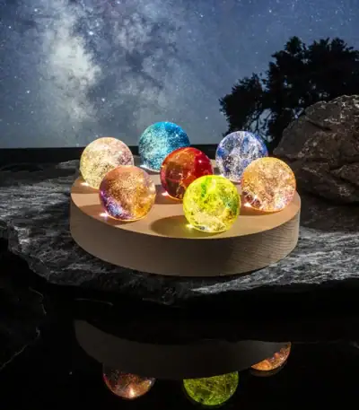 Collection de balles de cristal colorées illuminées, posées sur une surface rocheuse avec un ciel étoilé en arrière-plan, créant une ambiance magique et mystérieuse.