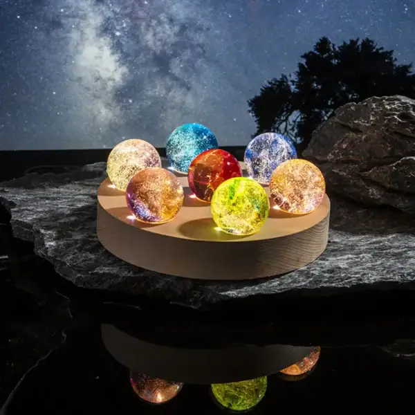 Collection de balles de cristal colorées illuminées, posées sur une surface rocheuse avec un ciel étoilé en arrière-plan, créant une ambiance magique et mystérieuse.