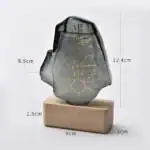 Pendentif en pierre gravée avec symboles mystérieux, posé sur un socle en bois, dimensions visibles pour une meilleure compréhension.